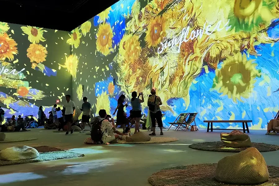 Besucher in einem immersiven Kunstmuseum mit Projektionen von Van Goghs Sonnenblumen auf den Wänden.